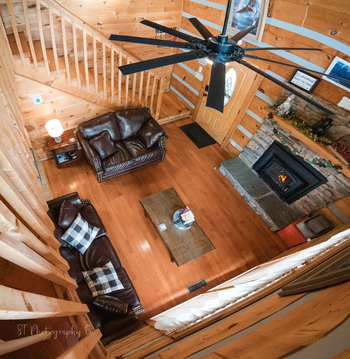 This image features a warm and inviting living area with a leather sofa, fireplace, coffee table, staircase, and visible front door. The space appears open and easy to navigate, suggesting a welcoming and accessible environment for guests of all abilities. The front door's proximity to the main living area hints at a layout that minimizes barriers to entry and movement.