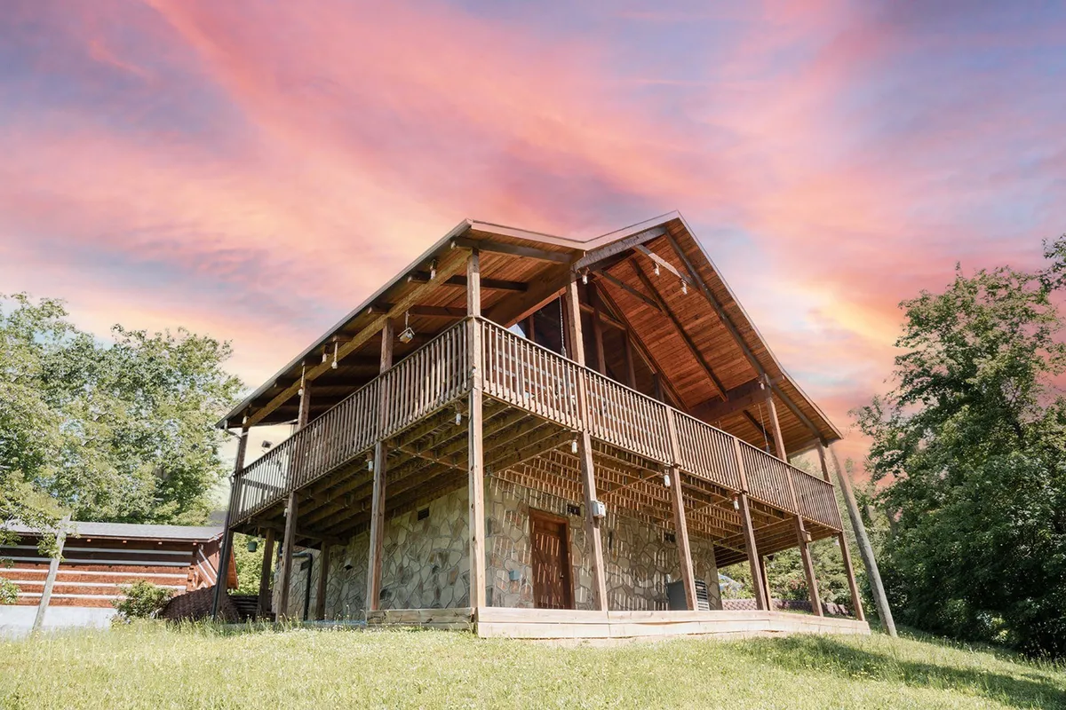 The cabin’s stone exterior and wooden balcony are showcased with a dramatic sky in the background. The inviting balcony hints at relaxation and a strong connection to the outdoors.