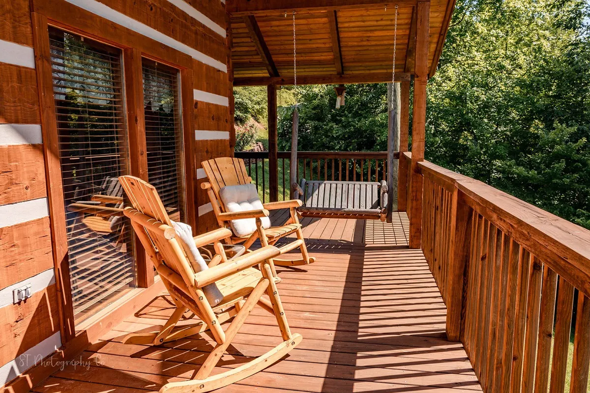 This exterior image features inviting wooden rocking chairs and a swing set on a wide porch, surrounded by lush greenery. The setting is tranquil and ideal for relaxing outdoors while enjoying the fresh air with your pet nearby.